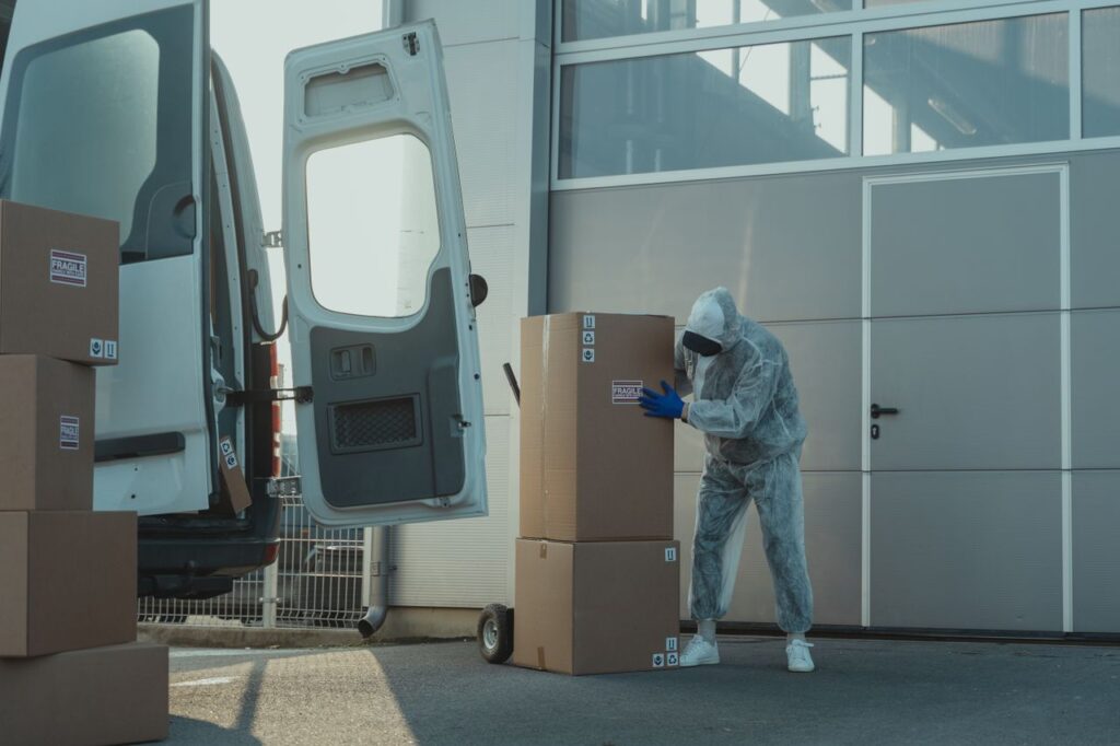A delivery worker in PPE handling cardboard boxes outside a warehouse with a van.